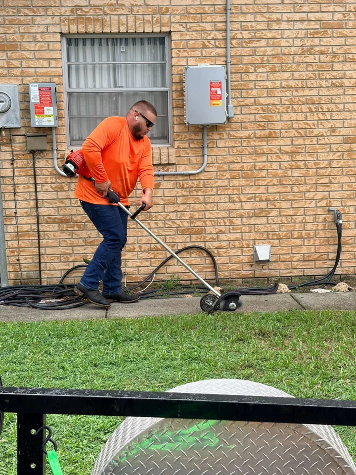 Crew member using an edger on a sidewalk beside a brick building